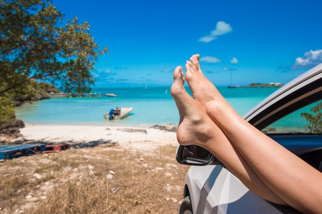 Female barefoot from the window of a car on tropical beach