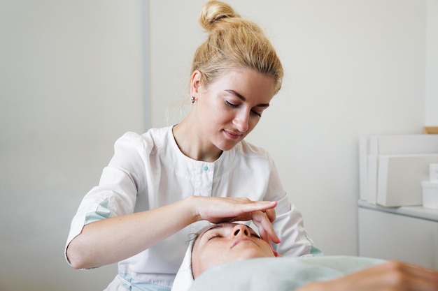 Female beautician doing facial massage her female client in a beauty clinic