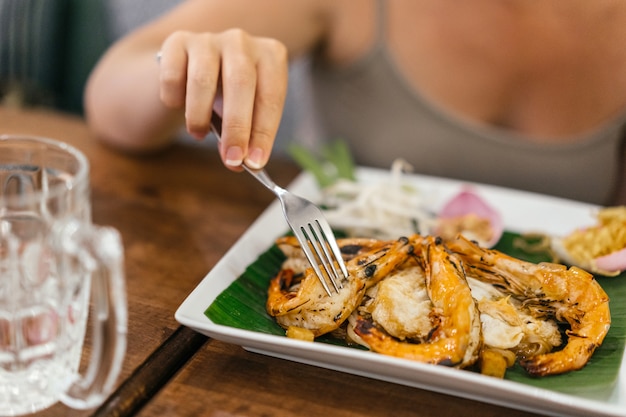 Photo female beautiful hand with manicure holds a fork over shrimps with rice and spicy sauce.