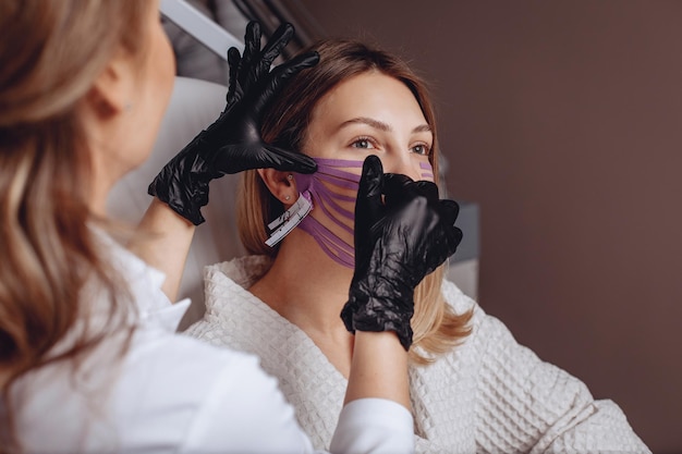 The female in the beauty salon's office receives a taping procedure to tighten the skin of her face