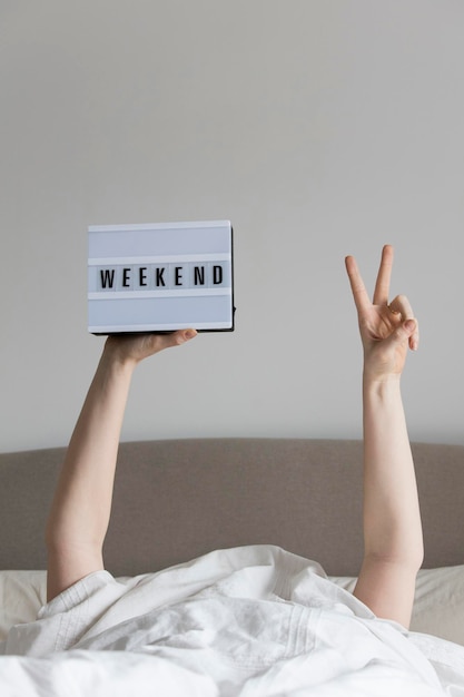 Female in bed under the sheets holding a weekend sign