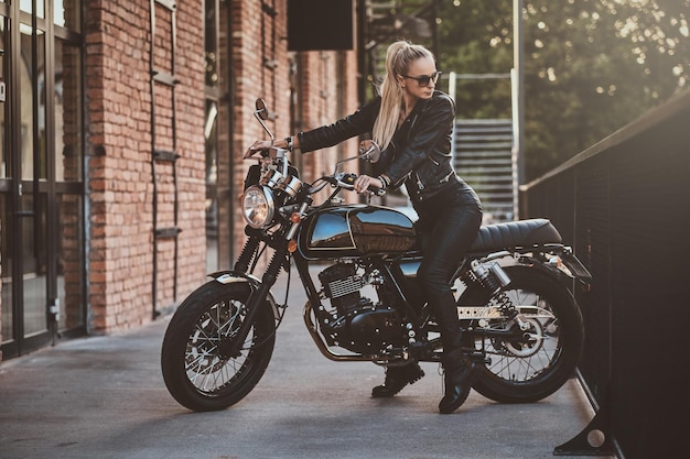 Female biker in full leather suit is posing for photographer while sitting on her brand new motorbike.