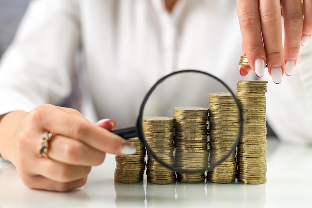 Female boss looking through a magnifying glass at a stack of coins on the table