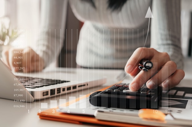 Female businessman calculates financials with graph paper on the laptop computer on the cost of home office.