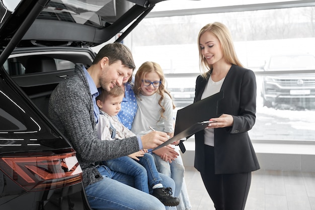 Female car dealer signing contract with client in auto salon