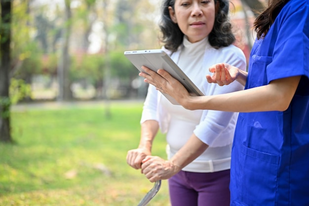 Female caregiver is talking and showing something on her tablet screen to an old lady