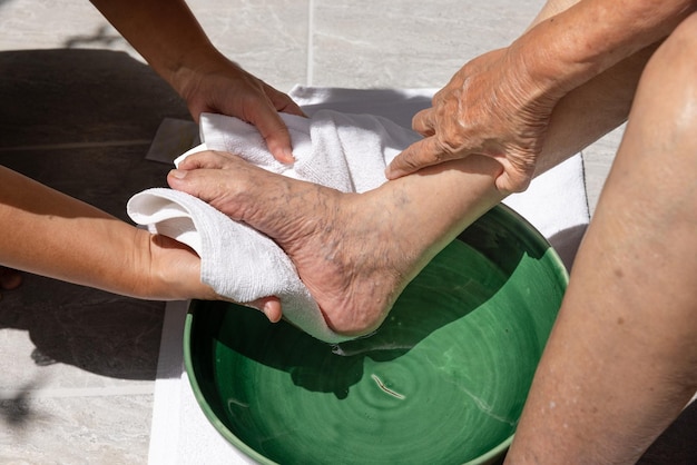 Female caregiver wipes the elderly woman feet by towel