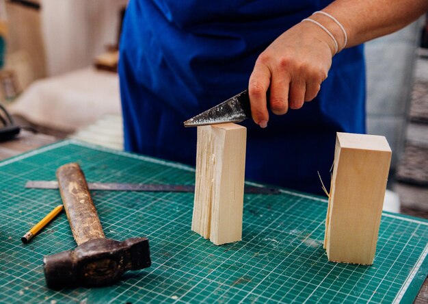 A female carpenter cuts wood with a knife in a carpentry or makeshift workshop Dust and shavings scatter in the air