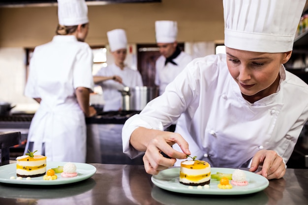 Female chef garnishing delicious desserts in a plate