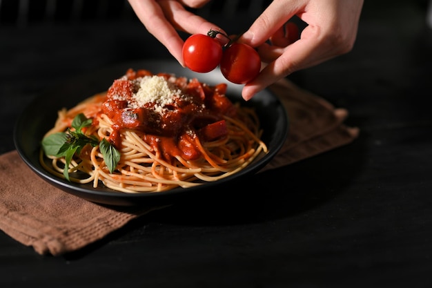 Female or chef hands putting some fresh tomato on a plate of spaghetti Italian pasta cuisine