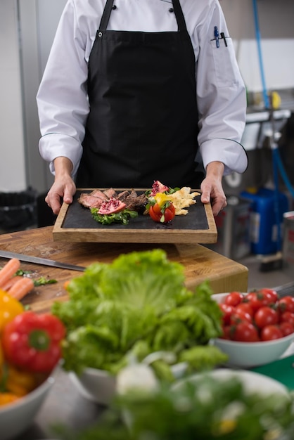 female Chef  in hotel or restaurant kitchen holding grilled beef steak plate with vegetable decoration