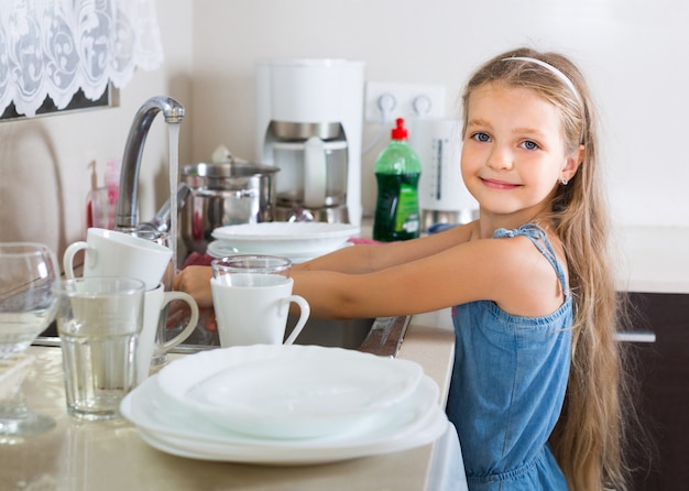 female child cleaning dishware at home