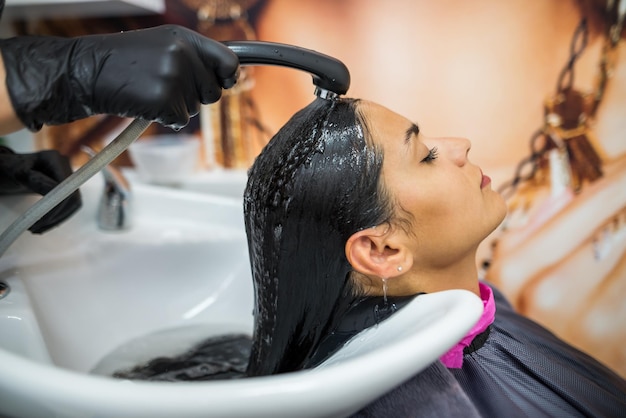 Female client washes hair in salon professional hairdresser washes head of female client with water and shampoo treatment hairstyle beauty hair care fashion service