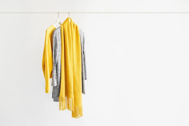 Female clothes in yellow and blue color on hanger on white background.  Jumper, shirt and scarf. Spring/autumn outfit. Minimal concept.