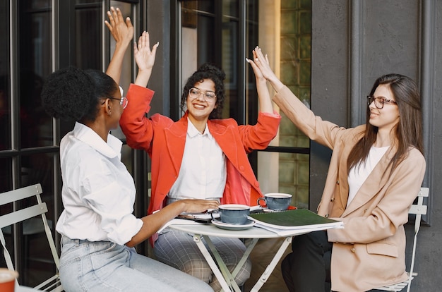 Female colleagues discussing data in the cafe outdoor. Multiracial female persons analyzing productive strategy for business projecting using documents in street cafe