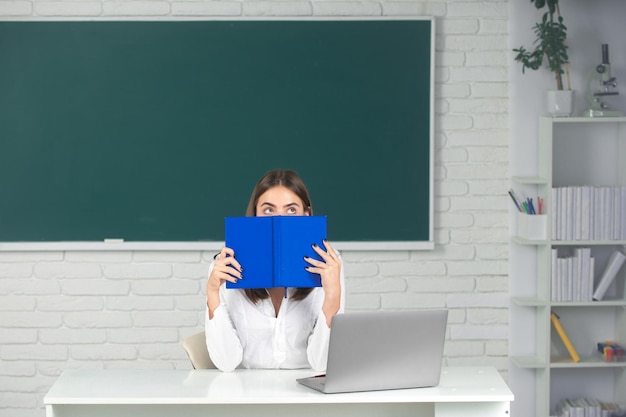 Female college student hiding behind an open book and looking away girl covering face with book