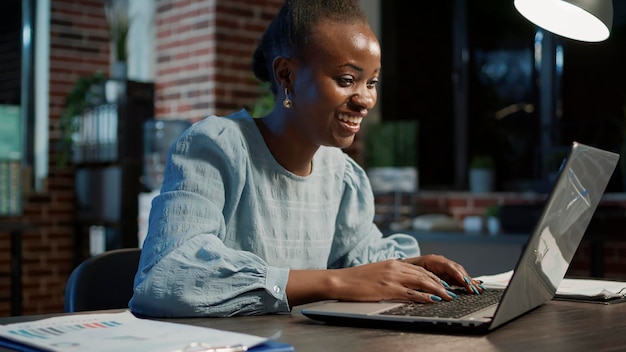 Female consultant celebrating share market exchange success on laptop, feeling happy. Working at night to analyze stock trade numbers for financial investment and hedge fund strategy.