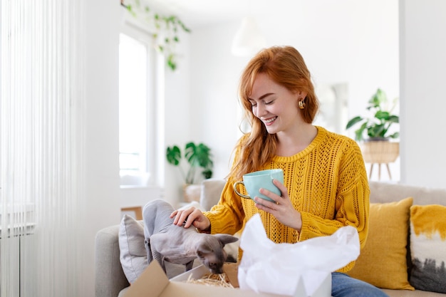 Female consumer unpack parcel receive retail purchase fast postal shipping delivery concept Beautiful young woman is holding cardboard box sitting on sofa at home