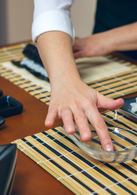 Female cook preparing sushi by wetting her hand in water to close the maki roll