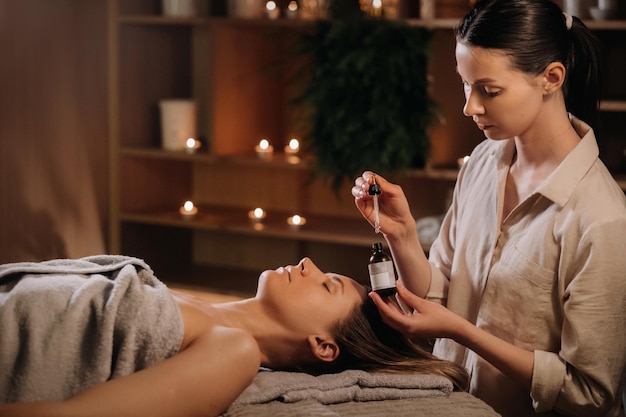 A female cosmetologist holds a pipette with essential oil before aromatherapy and massage to the patient aromatherapy