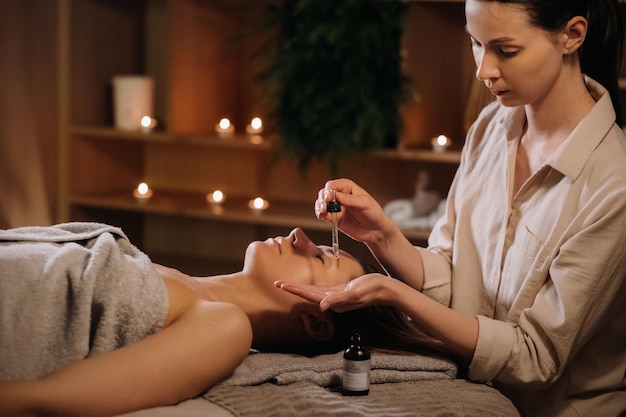 A female cosmetologist holds a pipette with essential oil before aromatherapy and massage to the patient aromatherapy