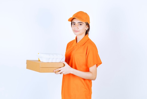 Female courier in orange uniform holding a white takeaway box with a cardboard parcel