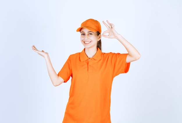 Female courier wearing orange uniform and cap showing ok hand sign.