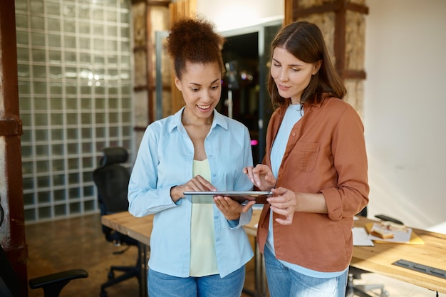 Female coworkers planning strategy on digital tablet standing in coworking office