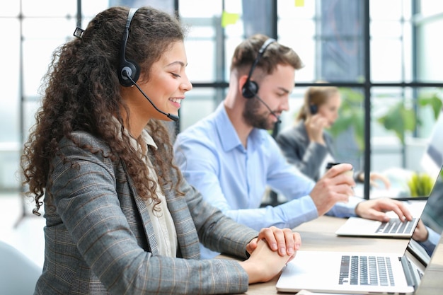 Female customer support operator with headset and smiling with collegues at background