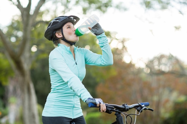 Female cyclist drinking water in forest