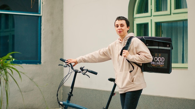 Female delivery worker waiting outside office building to deliver restaurant meal, carrying thermal backpack to give fastfood order to clients. Food delivery courier delivering lunch. Handheld shot.