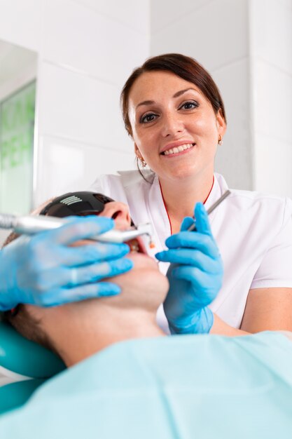 A female dentist examines the oral cavity of the patient with a tool with a mirror. Close-up portrait of a patient with a mouth open, a doctor in gloves holds a dental mirror.