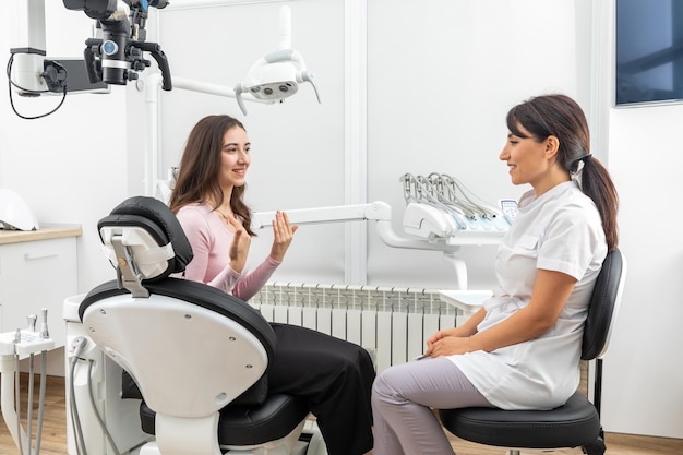 Female dentist talking to a young patient during appointment in modern dental clinic before teeth treatment