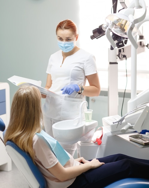 Female dentist with patient girl talking at dental clinic office