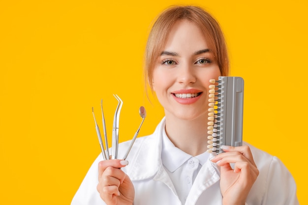 Female dentist with tools and teeth color chart on yellow surface