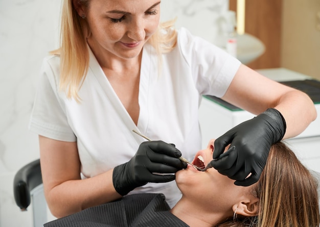 Female dentist at work with patient examining her teeth with dental tools