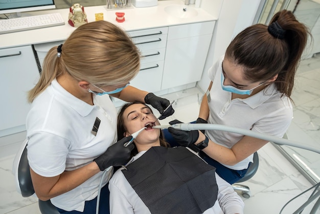 Female dentists treat the teeth of a young female patient with the latest equipment