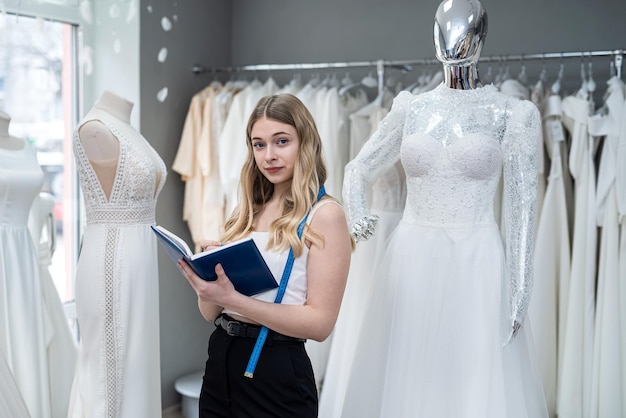 Female designer or seller making notes near dress in wedding fashion shop