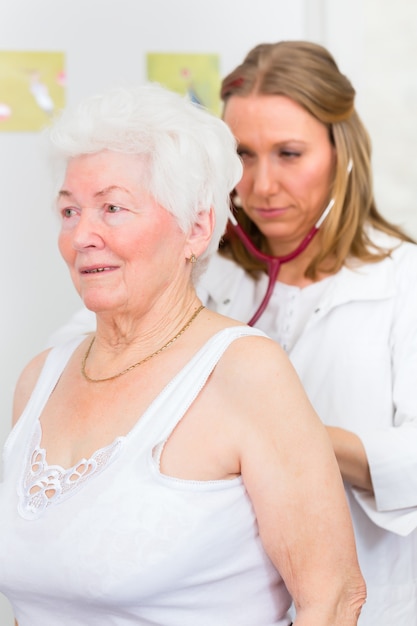 Female doctor auscultate breath and lungs of pensioner with stethoscope in surgery