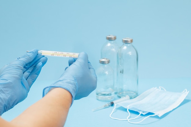 Female doctor in blue latex gloves holding a glass mercury thermometer