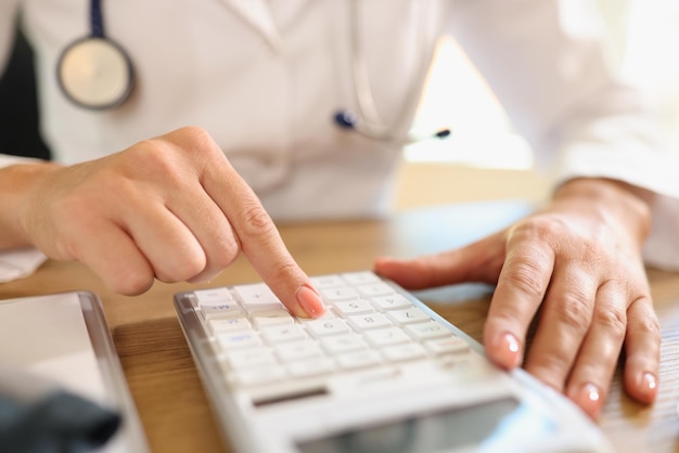 Female doctor counts price using calculator at her desk in medical clinic