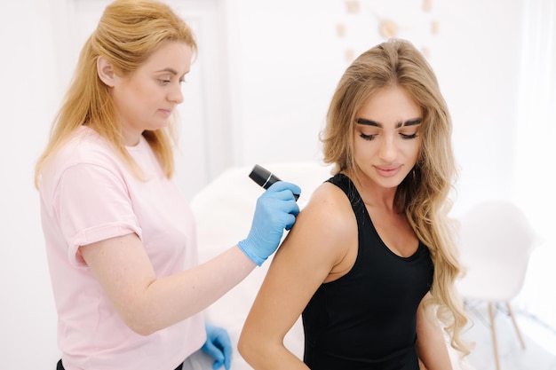 Female doctor dermatologist examines birthmarks and skin moles of the patient with a dermatoscope