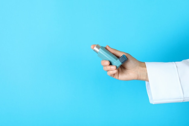 Female doctor hand holds asthma inhaler on blue background