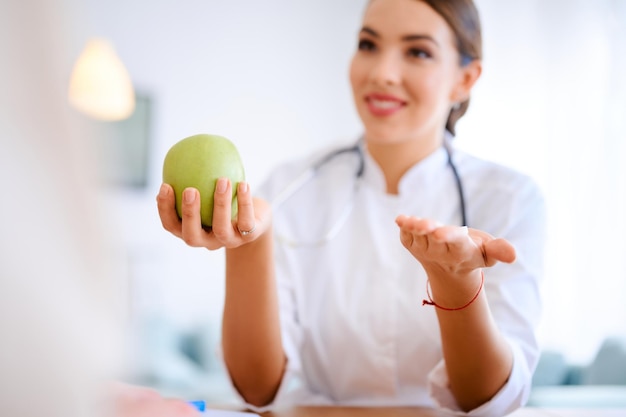 Female doctor holds apple and pills while discussing with patient in the office in hospital