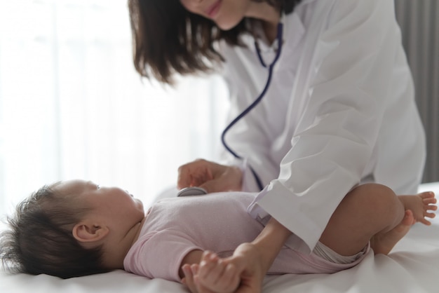 Female doctor is listening heart pulse rate of cute newborn baby on the bed by using stethoscope.