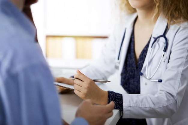 Female doctor and male patient discussing current health examination while sitting in sunny clinic, close-up. Medicine concept.