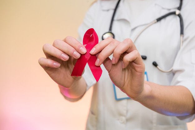 Female doctor in medical uniform holding red ribbon. AIDS day concept