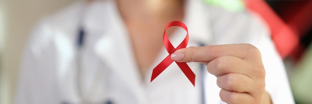 Female doctor in medical uniform holds red ribbon in her hands symbol of the fight against