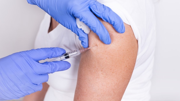 Female doctor or nurse giving shot or vaccine to patients shoulder closeup vaccination against flu p...