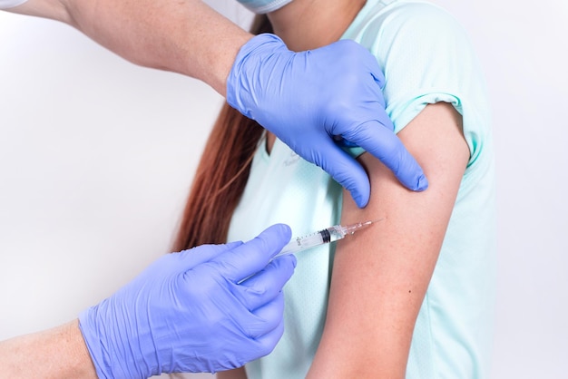 Female doctor or nurse giving shot or vaccine to patients shoulder young girl closeup vaccination